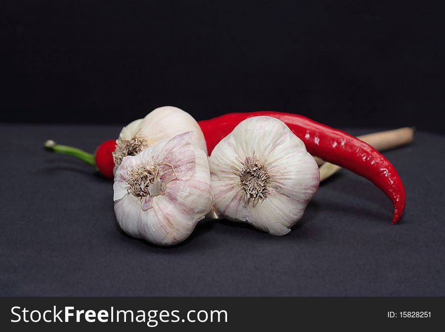 Few heads of garlic and one red chili pepper on dark background. Few heads of garlic and one red chili pepper on dark background