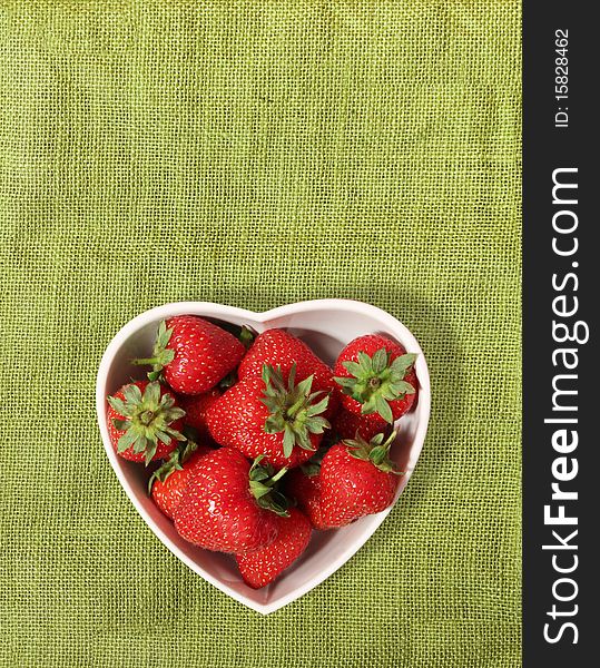 Strawberries in a heart shaped bowl on a green canvas background