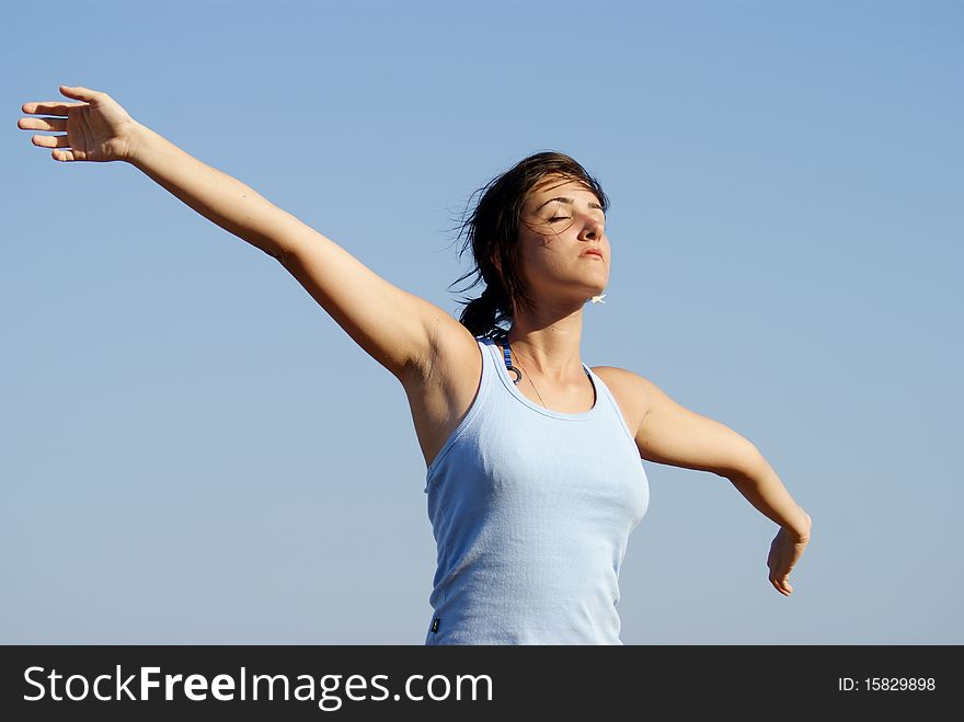 Portrait of a young beautiful woman spreading arms into the wind on a blue sky background. Portrait of a young beautiful woman spreading arms into the wind on a blue sky background