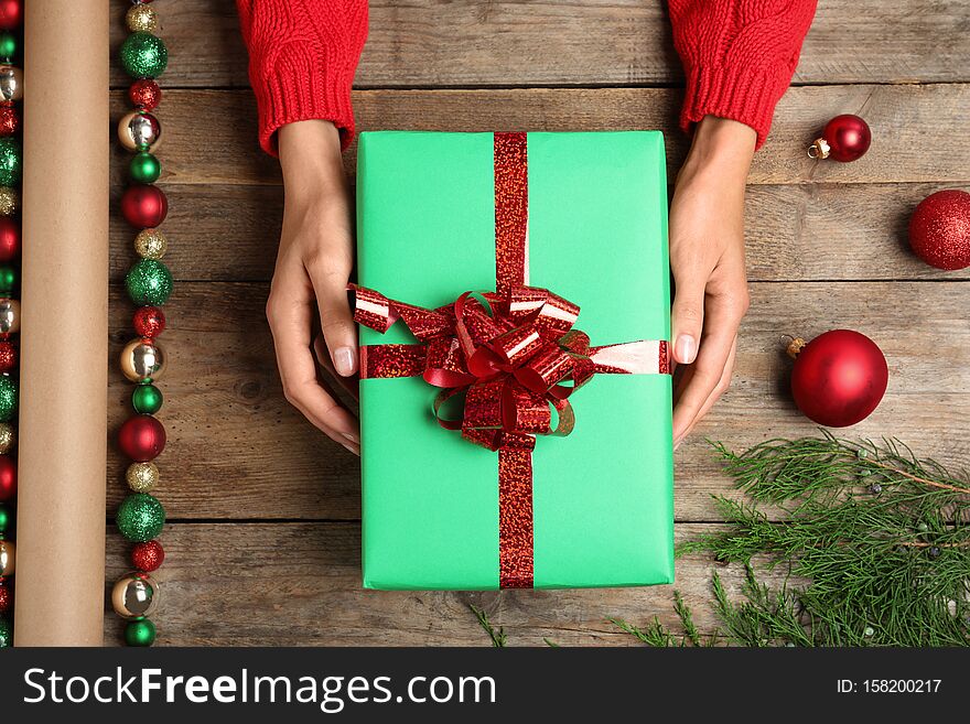 Woman wrapping Christmas gift at wooden table, top view