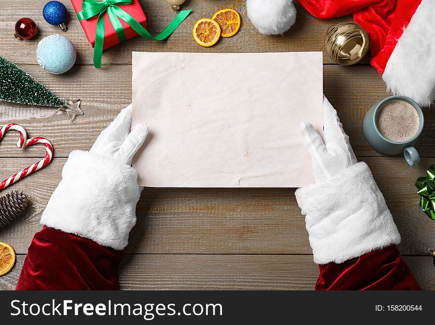 Santa Claus holding empty paper at wooden table, top view. Space for text