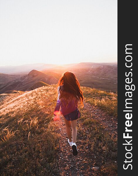 Happy young woman running on feather grass field in sunset light. Nature lifestyle and amazing view around. Long black hair with colored locks. Happy young woman running on feather grass field in sunset light. Nature lifestyle and amazing view around. Long black hair with colored locks