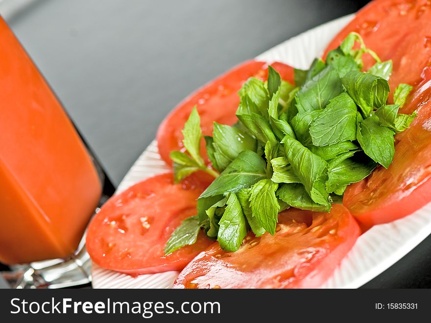 Tomato slices with green leaves and tomato juice in glass on black background