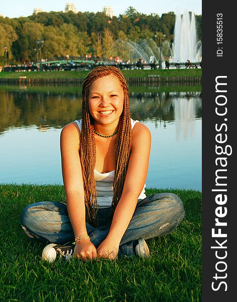 Pretty asian girl with braids smiles and sits on a grass. Pretty asian girl with braids smiles and sits on a grass