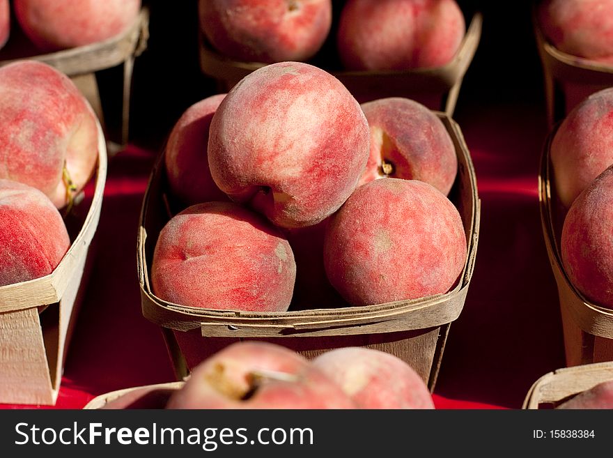 Peaches in a small wooden baskets on a red table cloth.