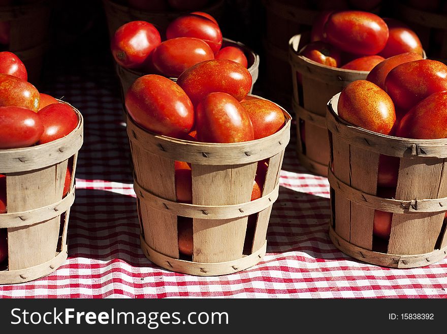 Tomatoes in a small wooden baskets on a red and white table cloth.