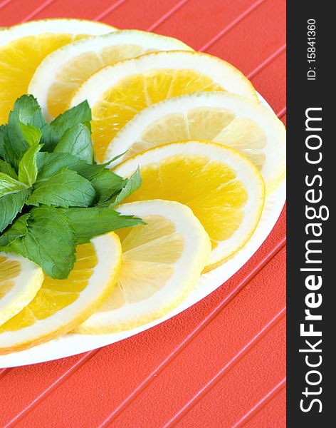 Slices of lemon and orange with mint leaves on red background