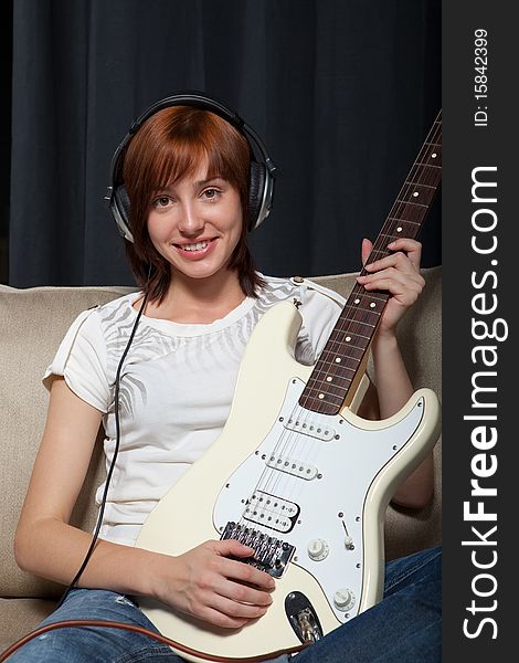 Teenage girl sitting on the sofa in headphones playing electric guitar.