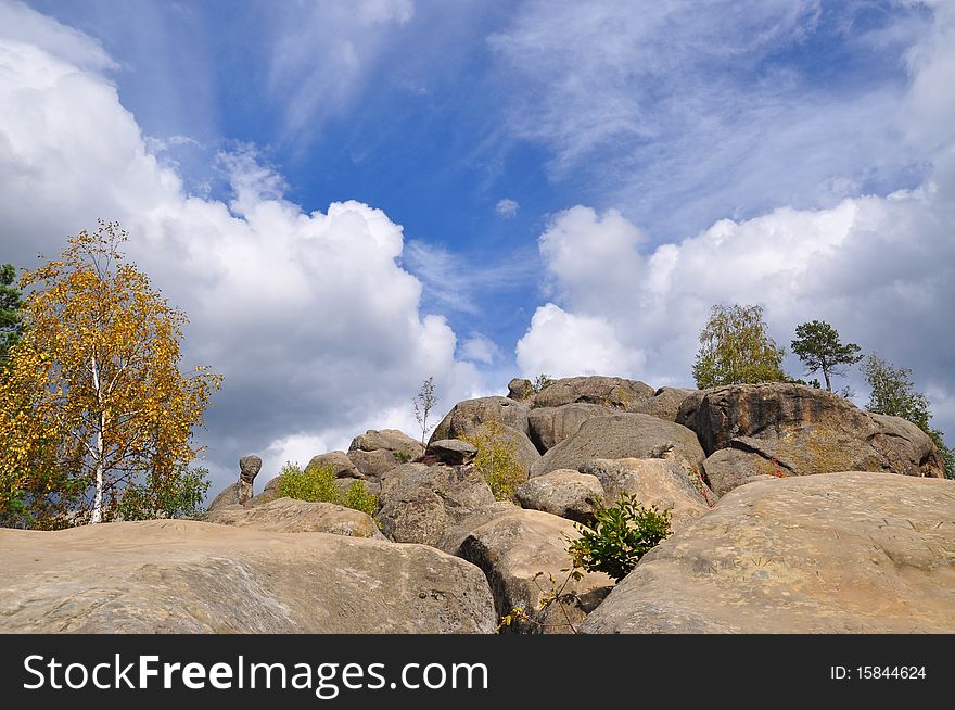 Trees on stones in an autumn mountain landscape under the dark blue sky in clouds
