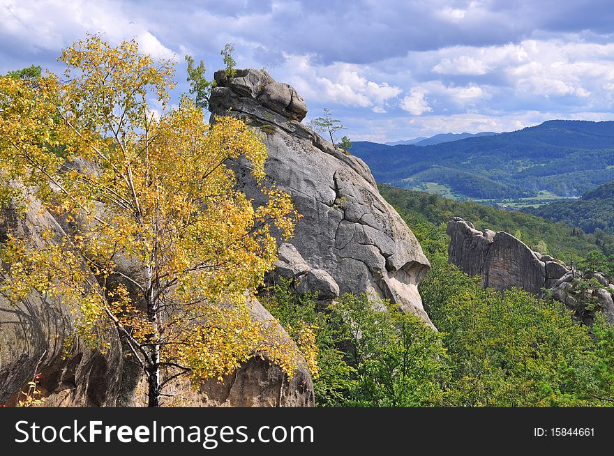 Rocks over wood in an autumn mountain landscape under the dark blue sky. Rocks over wood in an autumn mountain landscape under the dark blue sky