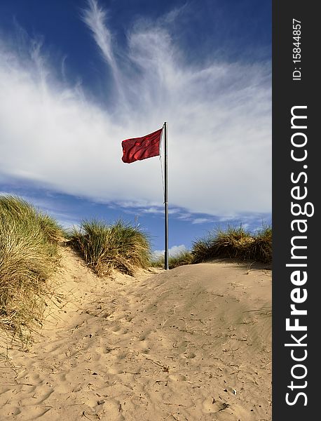A fluttering red warning flag on a sand dune. A fluttering red warning flag on a sand dune