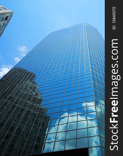 Glassy skyscraper of New York is photographed from below against blue sky. Next building and white cloud are reflected in its mirror surface. Glassy skyscraper of New York is photographed from below against blue sky. Next building and white cloud are reflected in its mirror surface.