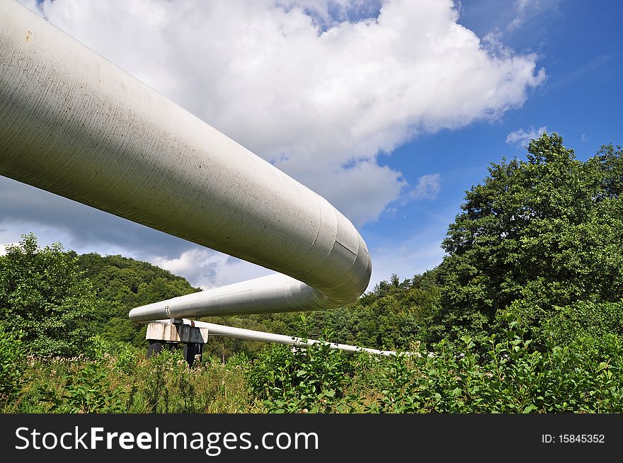 The high pressure pipeline in a summer landscape with the dark blue sky and clouds