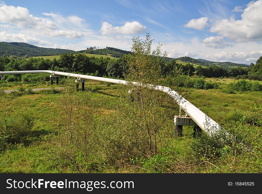 The high pressure pipeline in a summer landscape with the dark blue sky and clouds