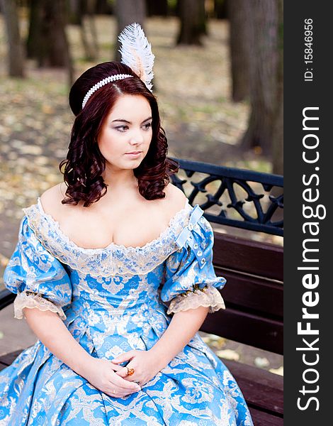 A portrait of lady in a blue baroque dress sitting on bench. A portrait of lady in a blue baroque dress sitting on bench