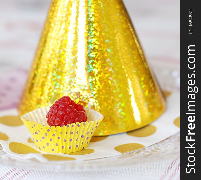 A single raspberry sittung on a plate next to party hat.