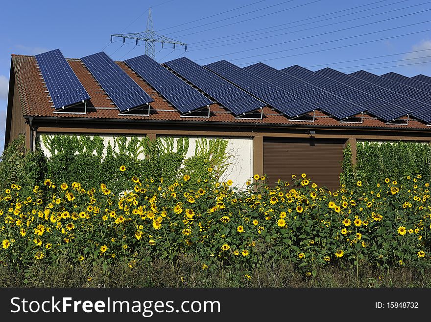 House with photovoltaic panels on its roof behind sun flowers. House with photovoltaic panels on its roof behind sun flowers.