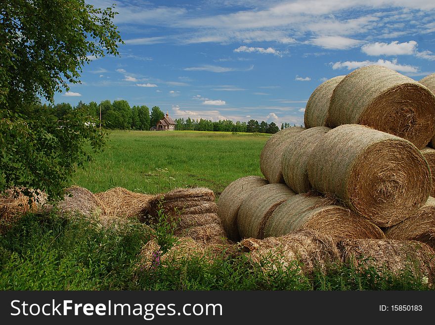 Meadows of Eastern Finland in Northern Savonia region, with Lonely ortodox wooden church, dried packed hay is at foreground