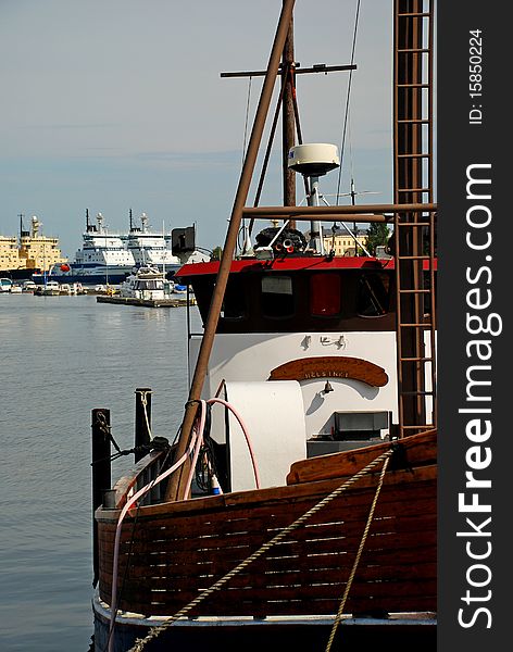 Traditional finish Fisher boat with wooden parts at Helsinki waterfront, the port with big ships is at the background. Traditional finish Fisher boat with wooden parts at Helsinki waterfront, the port with big ships is at the background