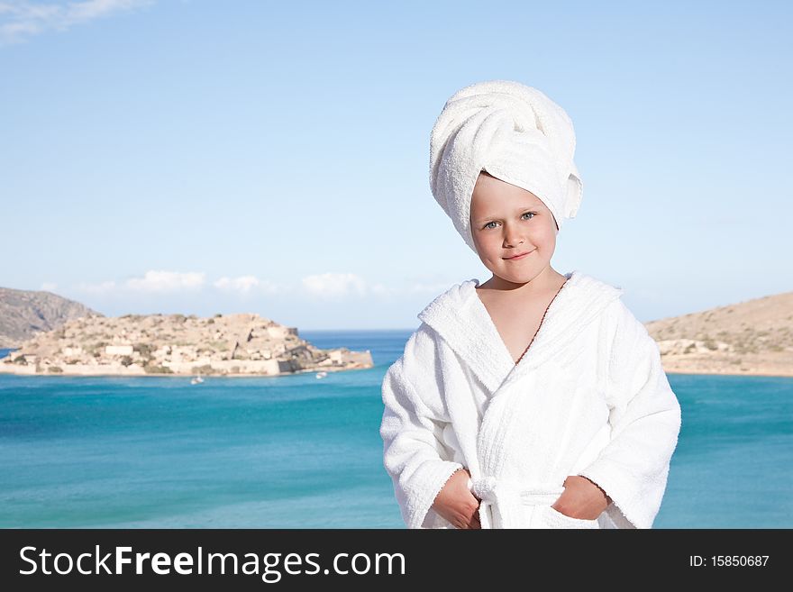 Portrait of happy smiling little girl with towel on the head in white bathrobe relaxing on terrace and looking at camera on the sea background. Portrait of happy smiling little girl with towel on the head in white bathrobe relaxing on terrace and looking at camera on the sea background