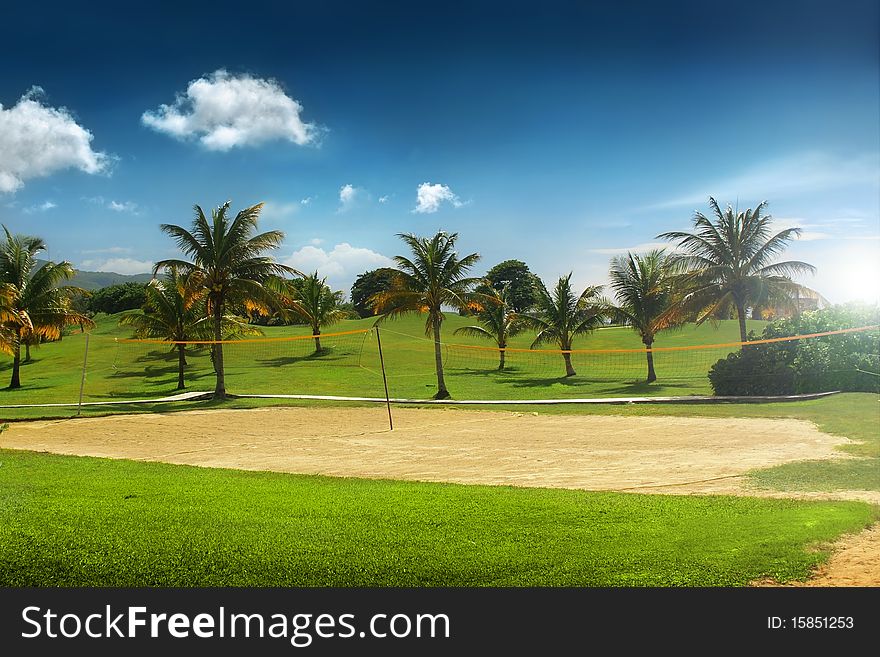 Beautiful tropical vacation resort with blue sky, volleyball court, and palm trees with green grass