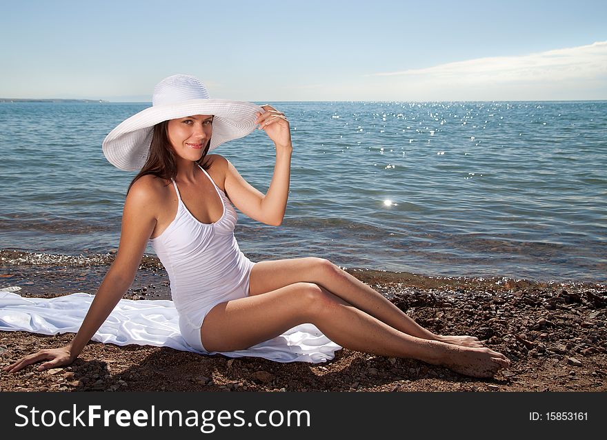 A beautiful young girl in a white hat on the beach happy smiles. A beautiful young girl in a white hat on the beach happy smiles