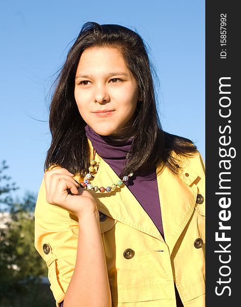 The young smiling woman in a yellow jacket and a bright beads against the blue sky. The young smiling woman in a yellow jacket and a bright beads against the blue sky
