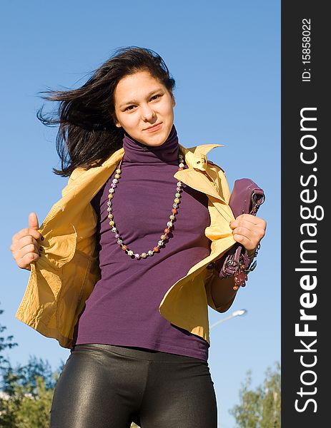 The young smiling woman in a yellow jacket and a bright beads against the blue sky. The young smiling woman in a yellow jacket and a bright beads against the blue sky