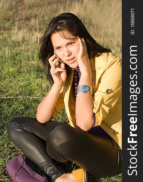 The young woman sits on a lawn and angrily speaks on the phone. The young woman sits on a lawn and angrily speaks on the phone