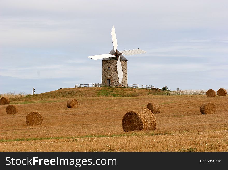 A windmill with white sails and hay in front of it, close to Mont-Saint-Michel, in France. A windmill with white sails and hay in front of it, close to Mont-Saint-Michel, in France