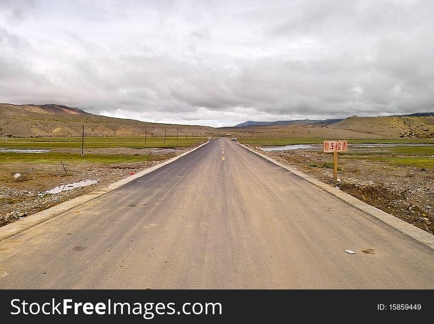 There is a asphalt road in ngari.the board say stop and examine near the road.