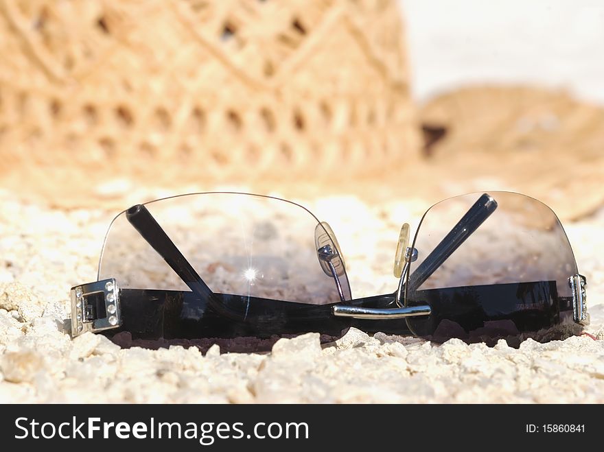 Sun glasses against a straw hat lie on sand. Sun glasses against a straw hat lie on sand