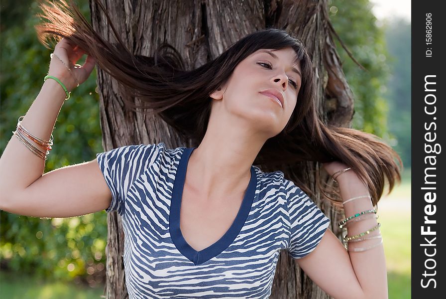 A portrait of a young woman in a blue and white zebra print top, standing outside beside a tree and flinging her hair back. A portrait of a young woman in a blue and white zebra print top, standing outside beside a tree and flinging her hair back.