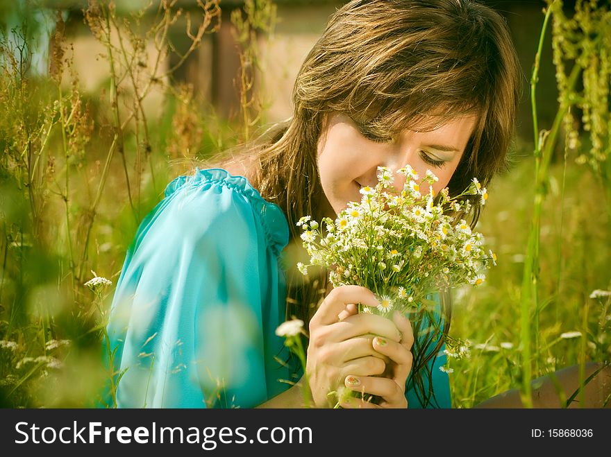 Beautiful girl sitting in a field with a bouquet of flowers
