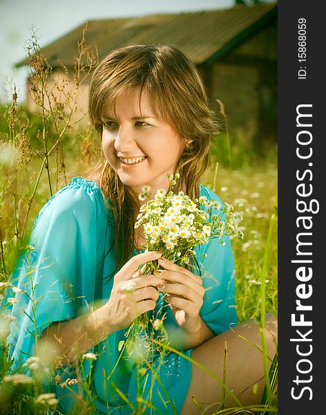 Beautiful girl sitting in a field with a bouquet of flowers