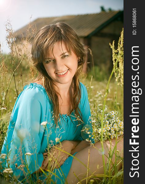 Beautiful girl sitting in a field with a bouquet of flowers