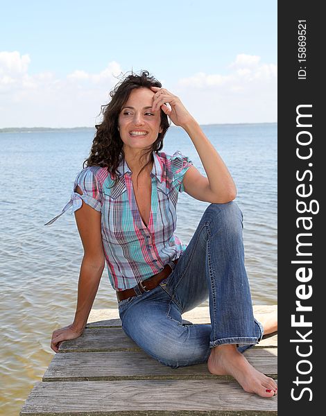 Woman sitting on a pontoon by a lake in summer. Woman sitting on a pontoon by a lake in summer