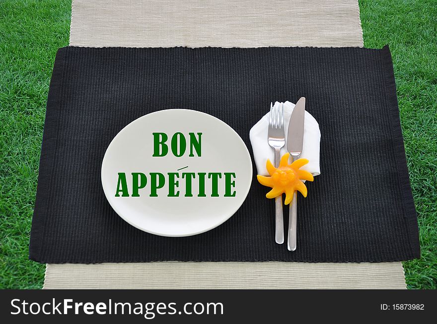 Place silverware placemat on grass with words bon appetite green text. Place silverware placemat on grass with words bon appetite green text