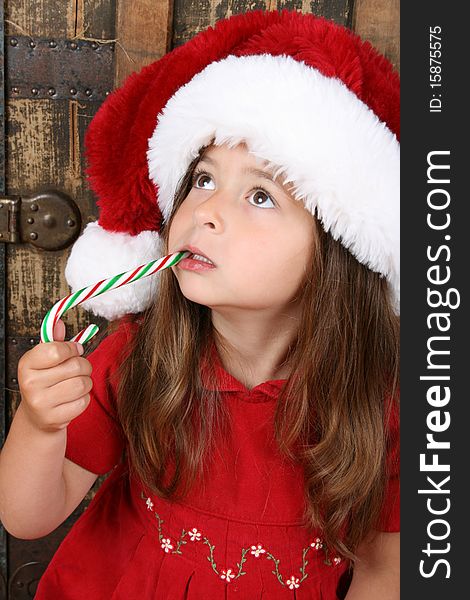 Cute brunette girl wearing a christmas hat, eating candy. Cute brunette girl wearing a christmas hat, eating candy