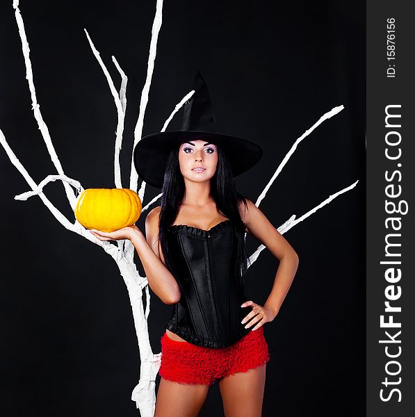 young brunette woman dressed as a witch with a pumpkin