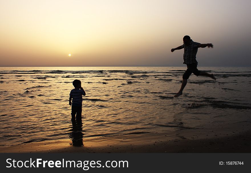 Silhouette image of father and his child by the sea shore, sunset