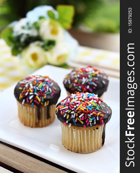 3 muffins on a white plate, placed on a brown table with table decoration and green background. 3 muffins on a white plate, placed on a brown table with table decoration and green background