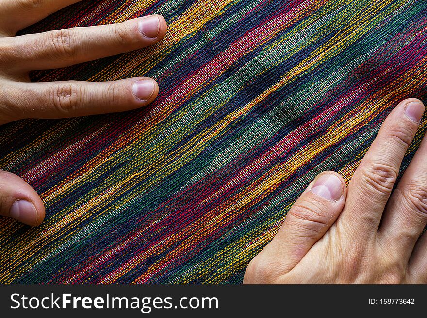 Man hands on motley striped fabric cloth material closeup. Tapestry background top view. Man hands on motley striped fabric cloth material closeup. Tapestry background top view