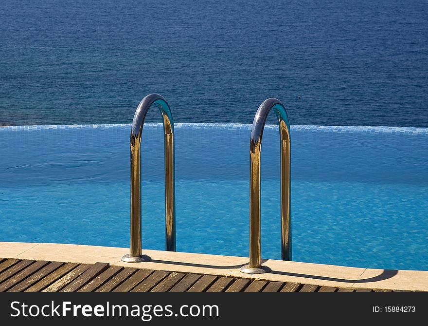 Shot of infinity swimming pool with handrails and blue sea in background. Shot of infinity swimming pool with handrails and blue sea in background