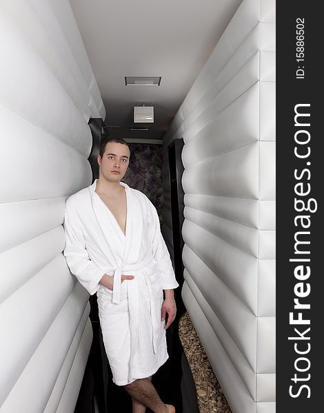 Handsome young man in spa corridor, wearing white towel robe