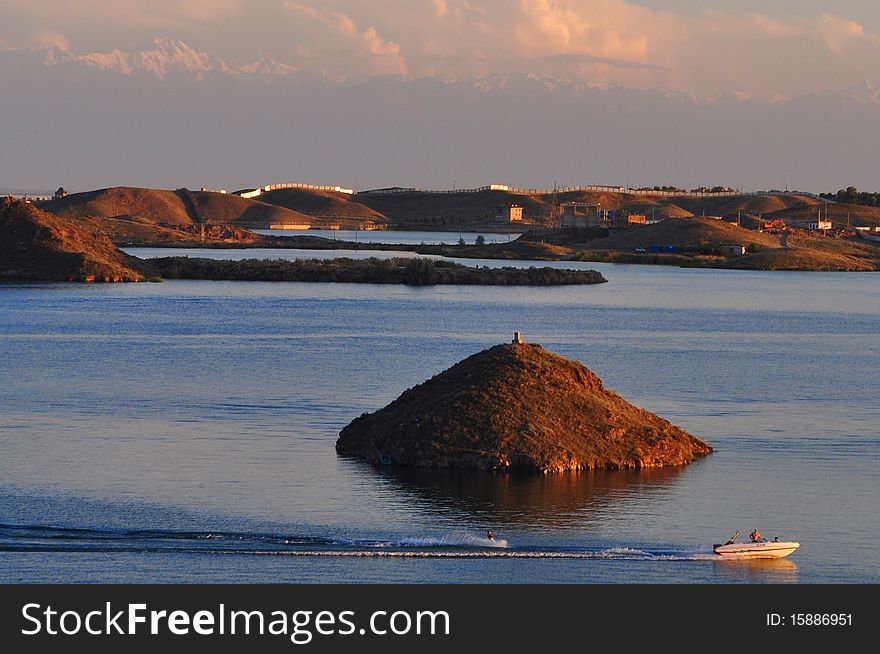 A speedboat zips across Kapshagai Lake in Alamty, Kazakhstan in the evening. The Tien Shan mountains in the background overlook the lake.