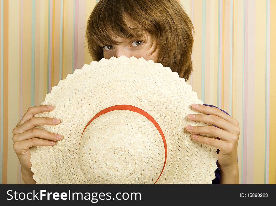 Beautiful girl on the background of a striped wall hides his face behind a straw hat. Beautiful girl on the background of a striped wall hides his face behind a straw hat