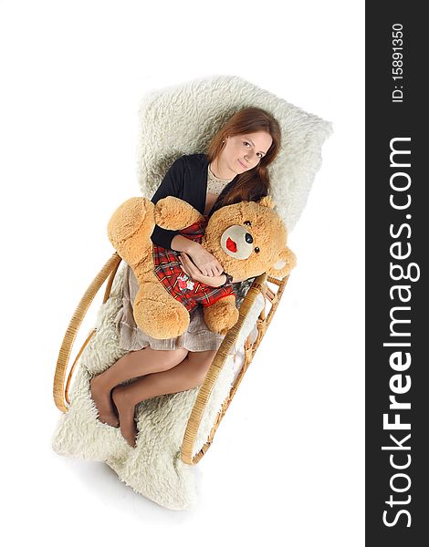 The girl sits in a rocking-chair on white background with a teddy bear in hands
