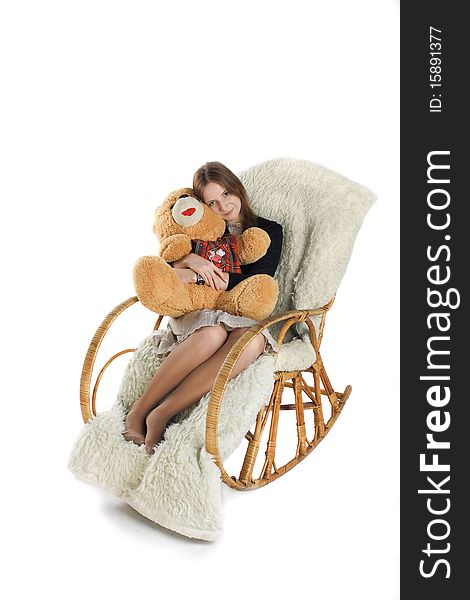 The girl sits in a rocking-chair on white background with a teddy bear in hands. The girl sits in a rocking-chair on white background with a teddy bear in hands