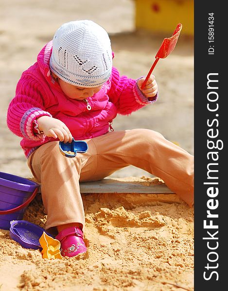 The little girl in a sandbox in a sunny day